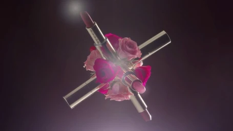 Four silver lipstick tubes arranged in an X shape interwoven with pink and magenta roses against a dark background