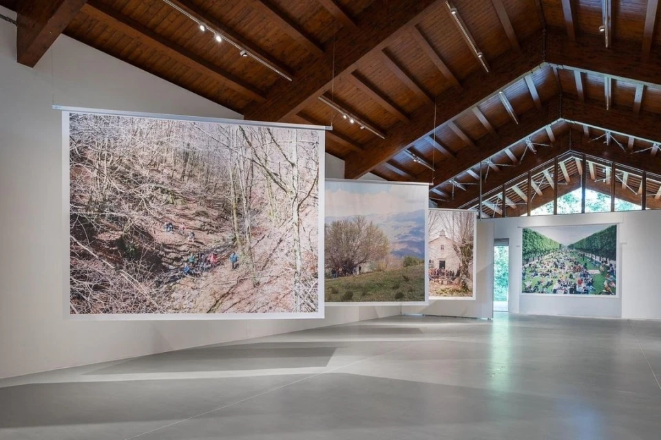 Interior view of art gallery showcasing photography exhibition with landscapes and group photos hanging in a bright, open space.