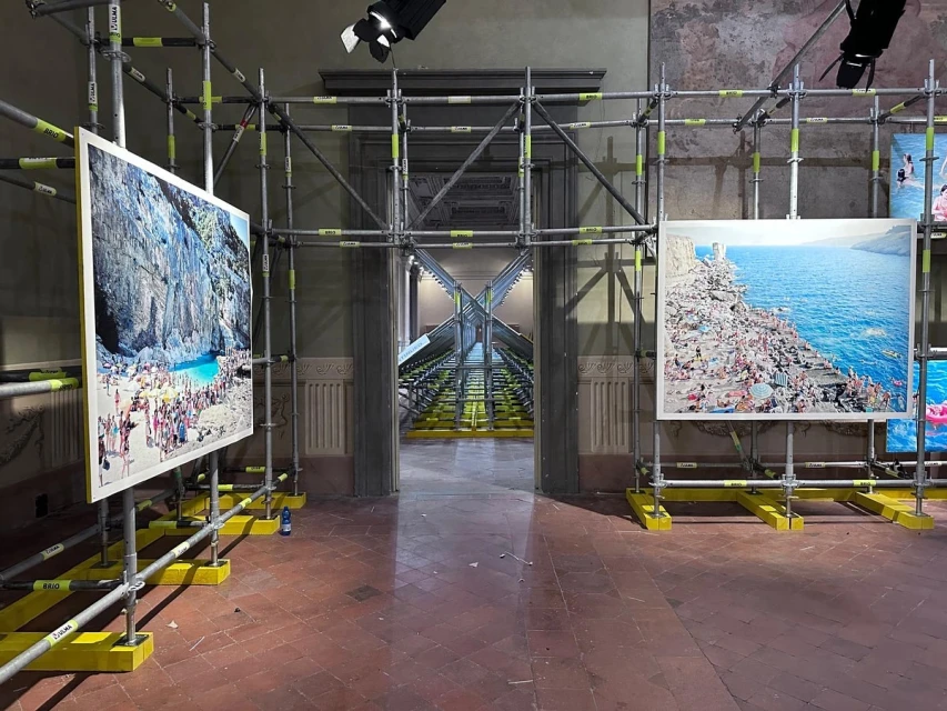 Art installation of large-scale beach photography on display, supported by scaffolding in gallery, featuring crowds on the shore.