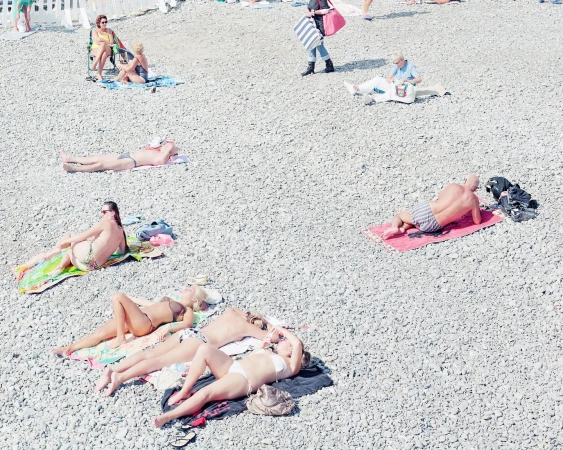 High-angle view of people sunbathing and relaxing on a pebble beach, enjoying the summer heat near the water's edge on a sunny day.