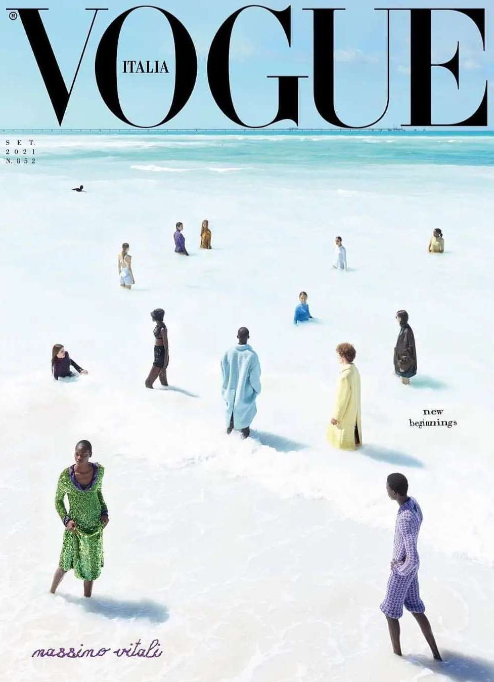 Vogue Italia magazine cover featuring a group of people standing in shallow water on a white sand beach with a clear blue sky above.
