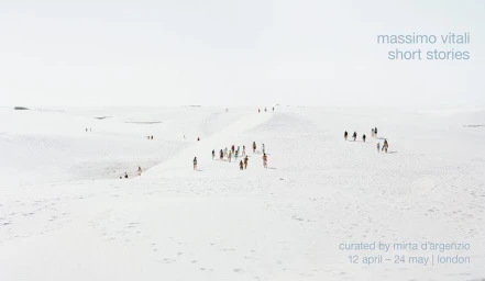 Distant figures walking across vast white sand dunes under an expansive pale sky, photographed by Massimo Vitali.