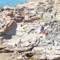 High-angle view of people relaxing and sunbathing on rugged rocky coastal formations by the water.