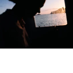 Silhouette of a person looking out a window at a calm ocean and distant islands at sunset
