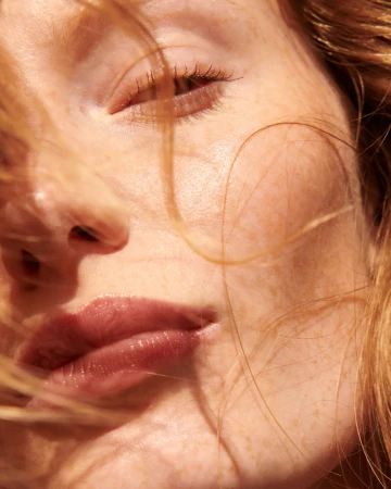 Close-up portrait of a woman with red hair, visible freckles, and natural makeup photographed by Mateusz Sitek.