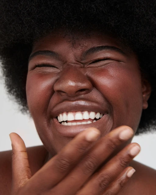 Close-up of a smiling African American woman with an afro, her hand near her face, conveying a joyful and expressive emotion in a studio setting.