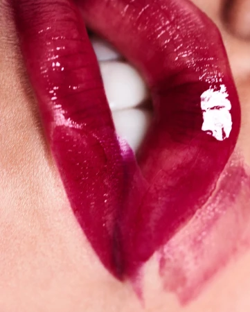 Close-up macro photography of glossy deep burgundy red lipstick on parted lips revealing white teeth by Mateusz Sitek