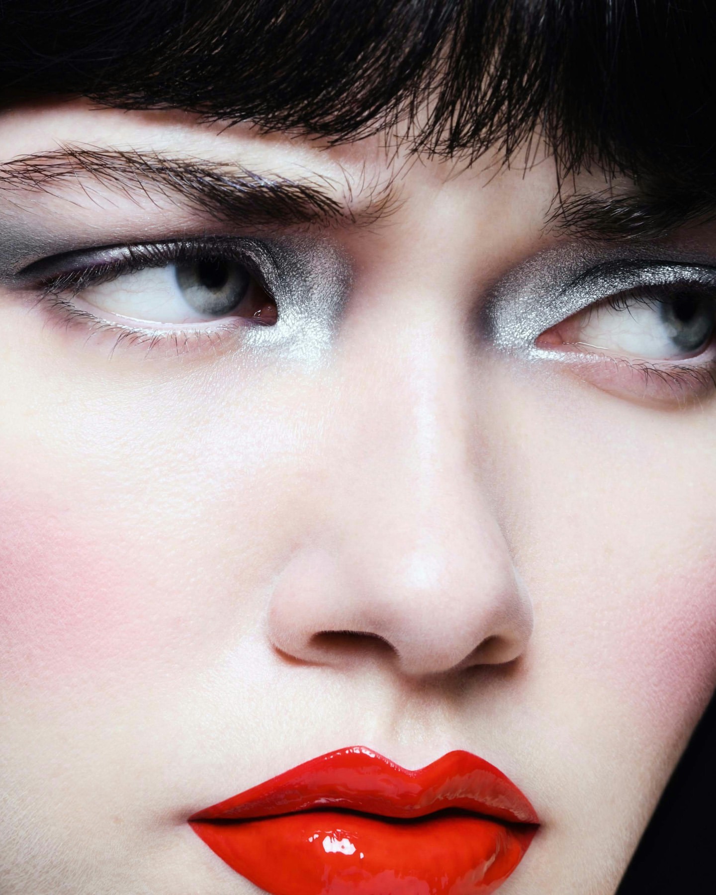 Close-up portrait of a woman with silver eyeshadow and bright red lipstick, looking to the side with a neutral expression.