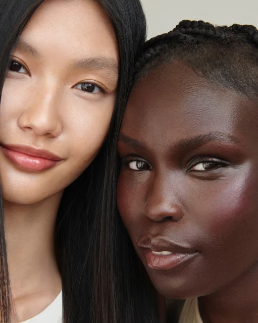 Close-up portrait of two women with radiant makeup. One Asian woman with long black hair and one African American woman with braided hair.