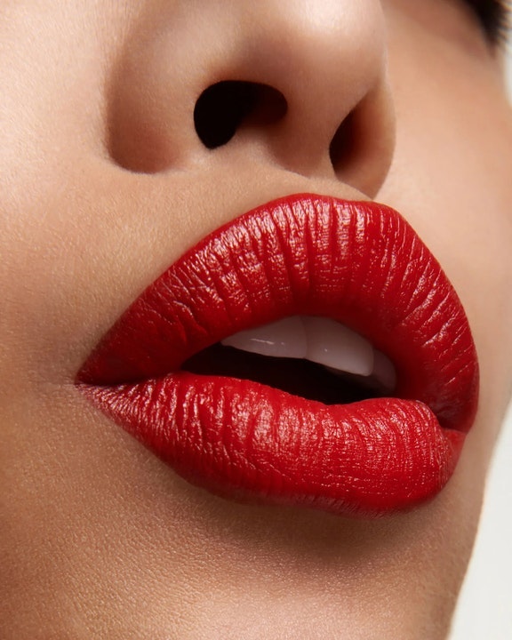 Extreme close-up of lips wearing vibrant red lipstick with teeth slightly showing