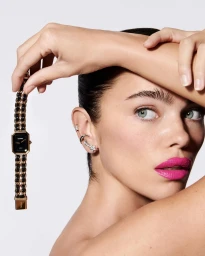 Close-up portrait of a woman with vibrant pink lipstick holding up a luxury gold chain watch by Mateusz Sitek.