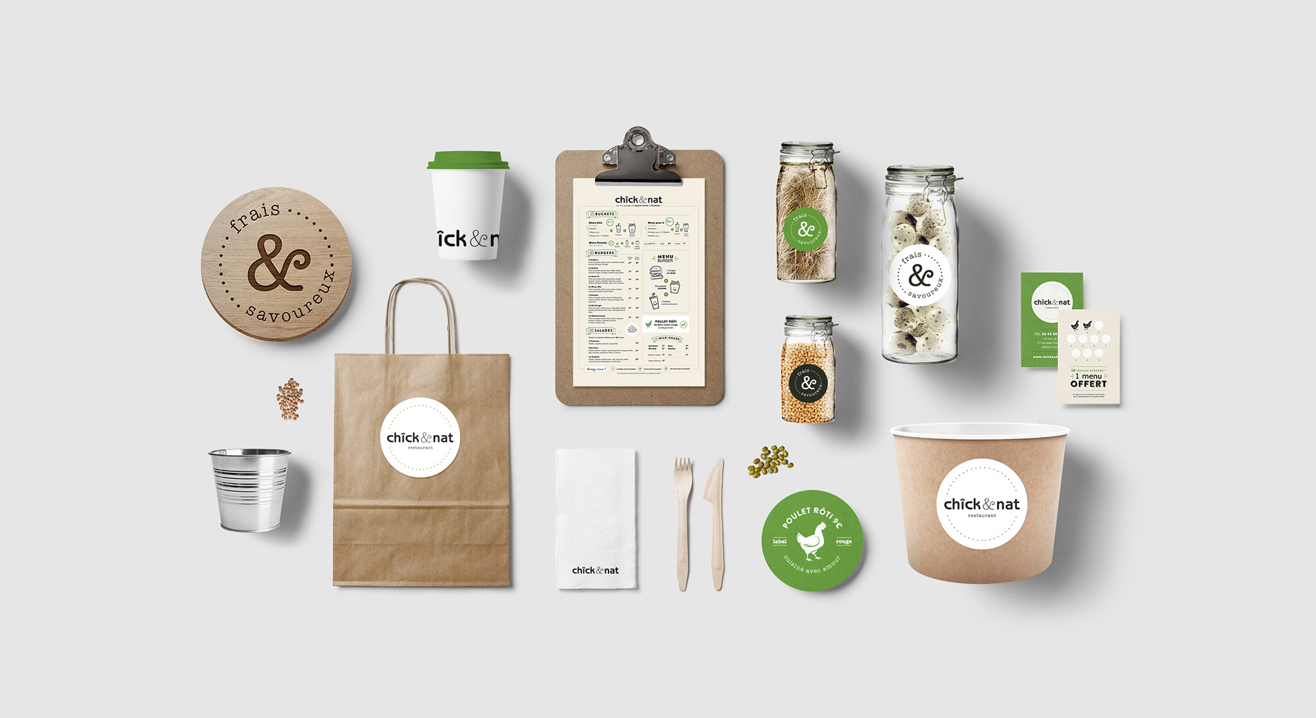 Overhead shot of Chick&Nat restaurant branding, including logo, takeout containers, menus, and wooden cutlery against a grey backdrop.