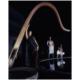 Three models posed at night near a curved sculpture and dark water pool in Paris by photographer Mathilde Agius.