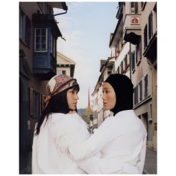 Two women in white tops posing on a narrow European street lined with traditional multi-story buildings.