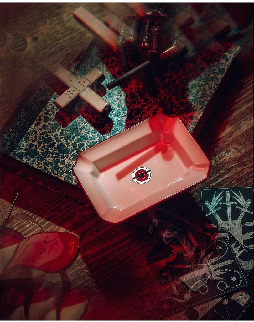 Overhead shot of an ash tray, cards, candle, wooden decoration and a book on a wooden surface with dark red and green hues.