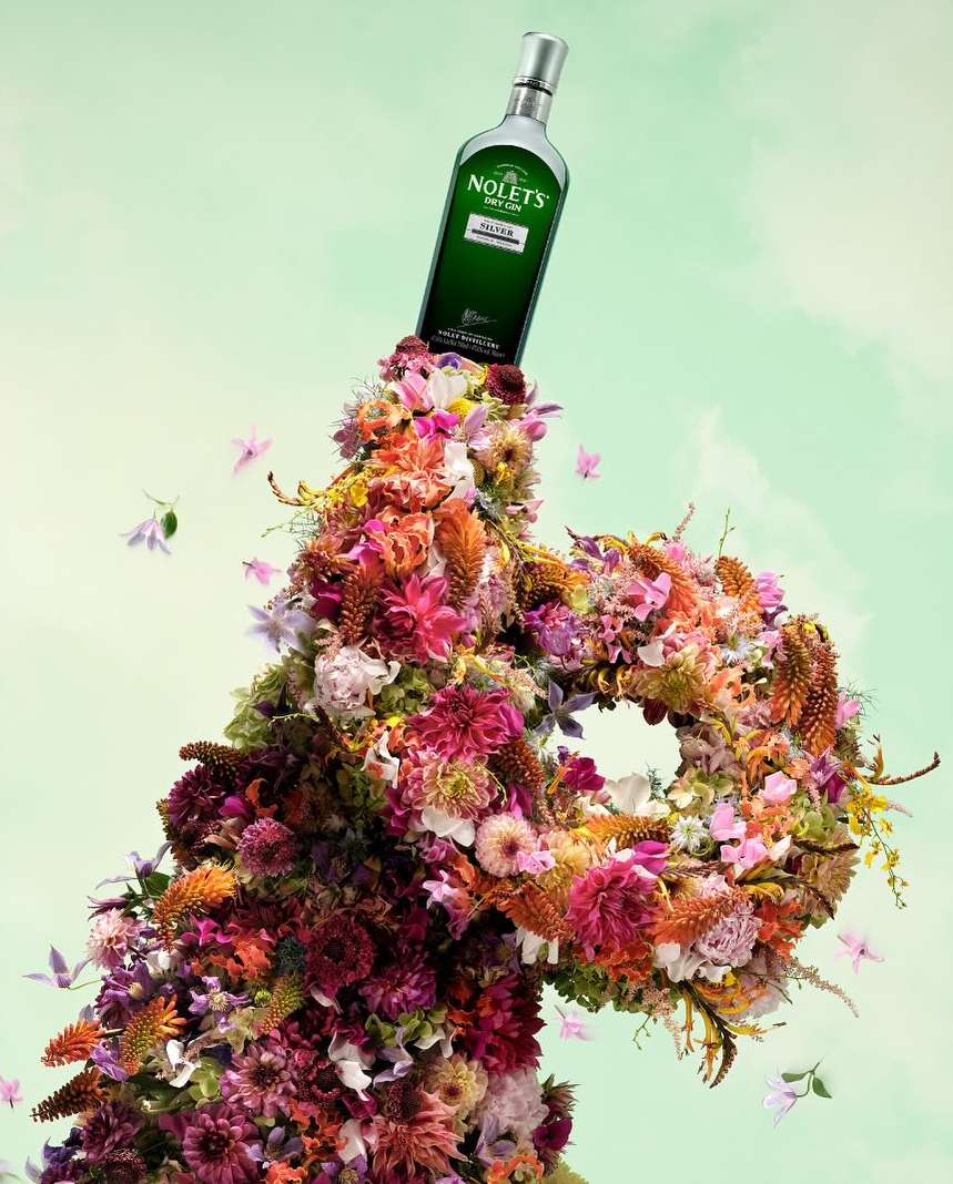 Still life shot of Nolet's gin bottle displayed on top of flower arrangement against a light green background, creating a botanical aesthetic.