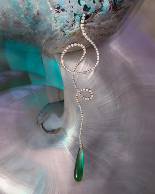 Elegant diamond necklace with a green teardrop pendant on a pearlescent seashell backdrop, creating a luxurious jewelry presentation.