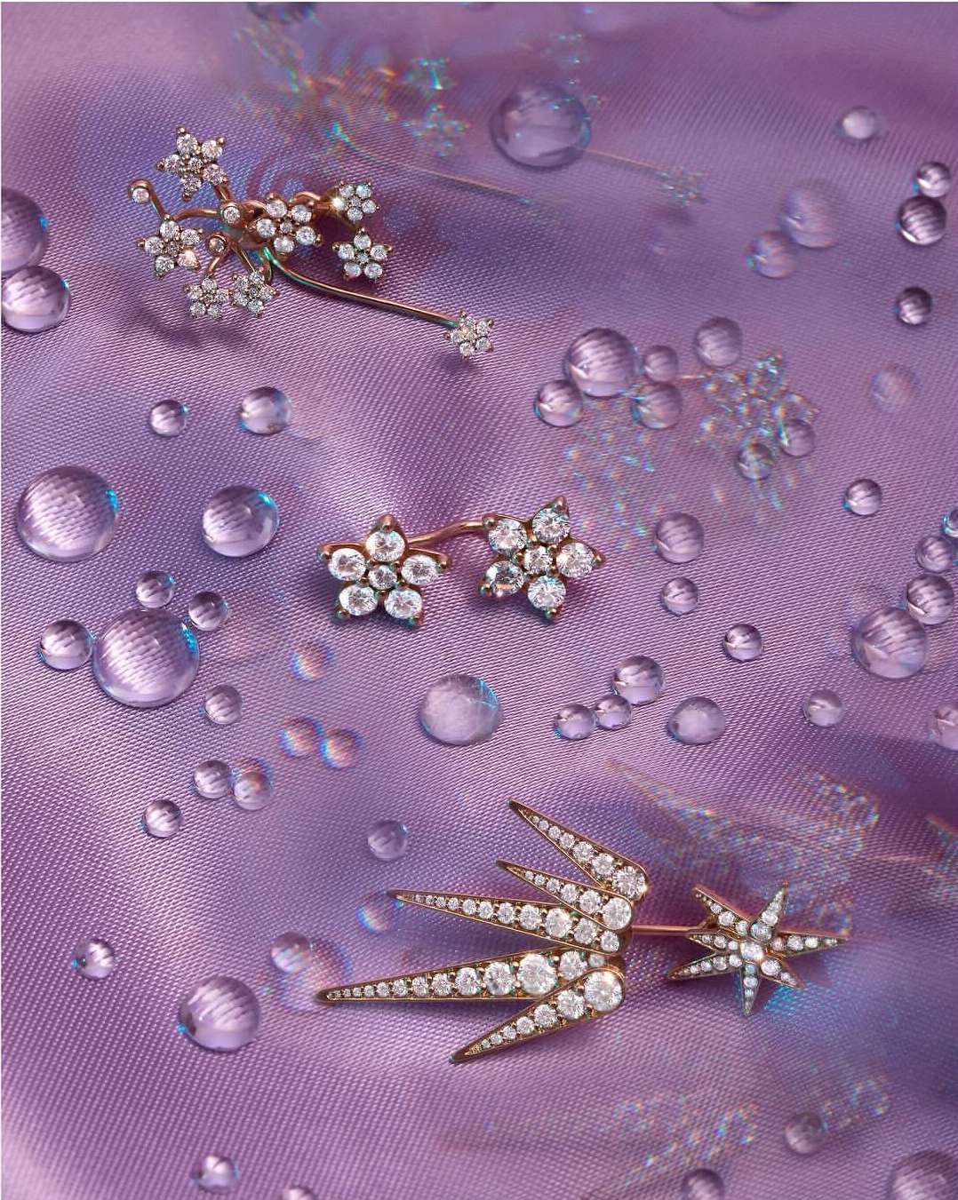 Elegant flower-inspired diamond earrings jewelry arranged on a textured purple fabric with water droplet accents for a glamourous aesthetic.