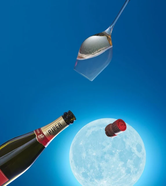 Celebratory image of a champagne bottle and glass with a cork flying mid-air against a bright blue background with a full moon.