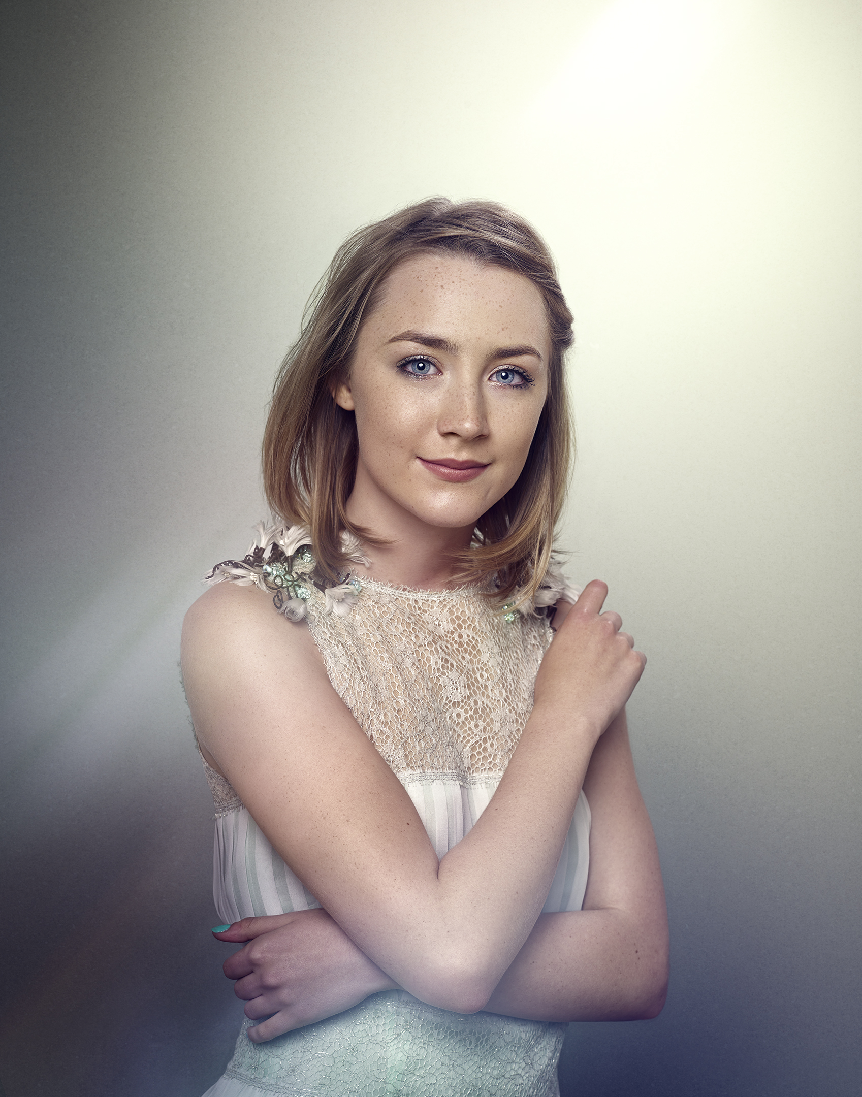 Portrait of a fair-skinned young woman with short blonde hair and blue eyes, wearing a sleeveless cream colored dress with floral accents.
