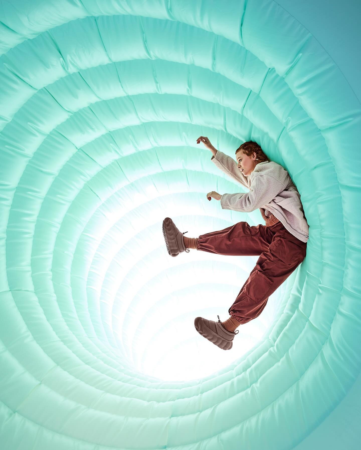A young adult female is positioned inside a light blue inflatable tunnel-like structure, wearing casual clothes and looking ahead.