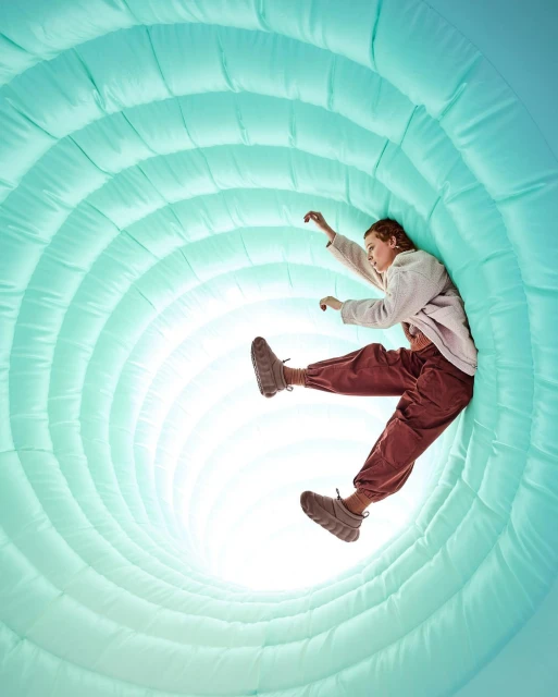 A young adult female is positioned inside a light blue inflatable tunnel-like structure, wearing casual clothes and looking ahead.