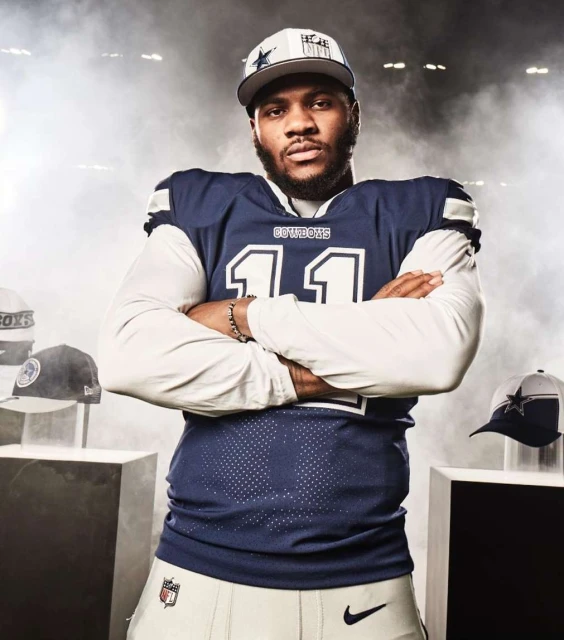 American football player in Dallas Cowboys uniform and hat poses in a studio with hats on display. Sports, fashion, and entertainment.