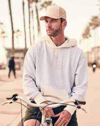 Man wearing a baseball cap and light-coloured hoodie sitting on a bicycle outdoors with palm trees in the background