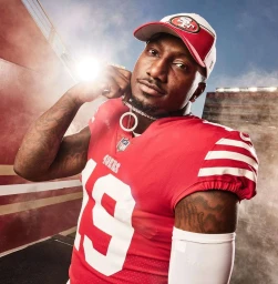 Football player wearing a red jersey and baseball cap holds a chain necklace in a stadium portrait by Matt Hawthorne.