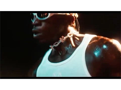 Adult male with dark skin wearing sunglasses and tank top, lit with blue and white light in dark indoor environment.