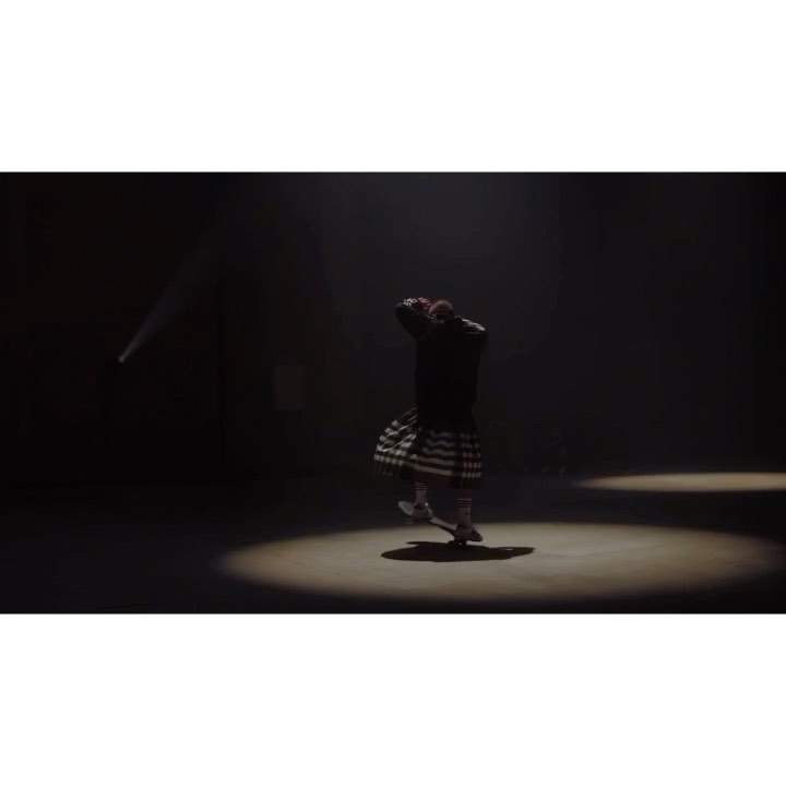 A dancer in a black jacket and patterned kilt performs in a spotlight against a dark background, showcasing movement and theatrical lighting.