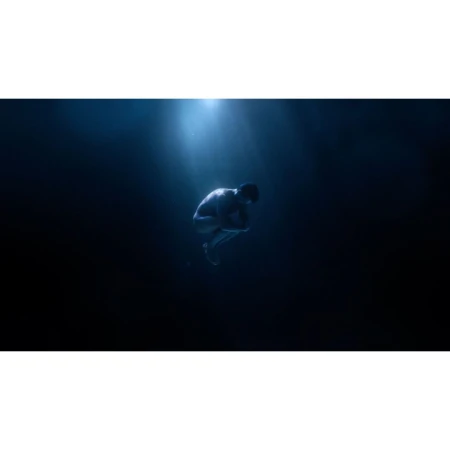 Adult male in fetal position underwater with bright light shining down on him, creating a mysterious and ethereal scene.
