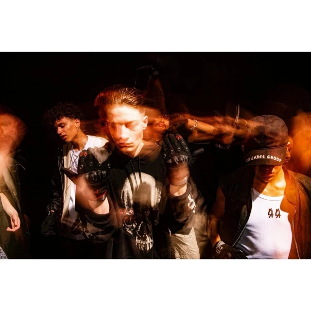 Group of young adults in urban scene at night, wearing fashion forward apparel with gloves, hats, and casual tops, with dynamic lighting.
