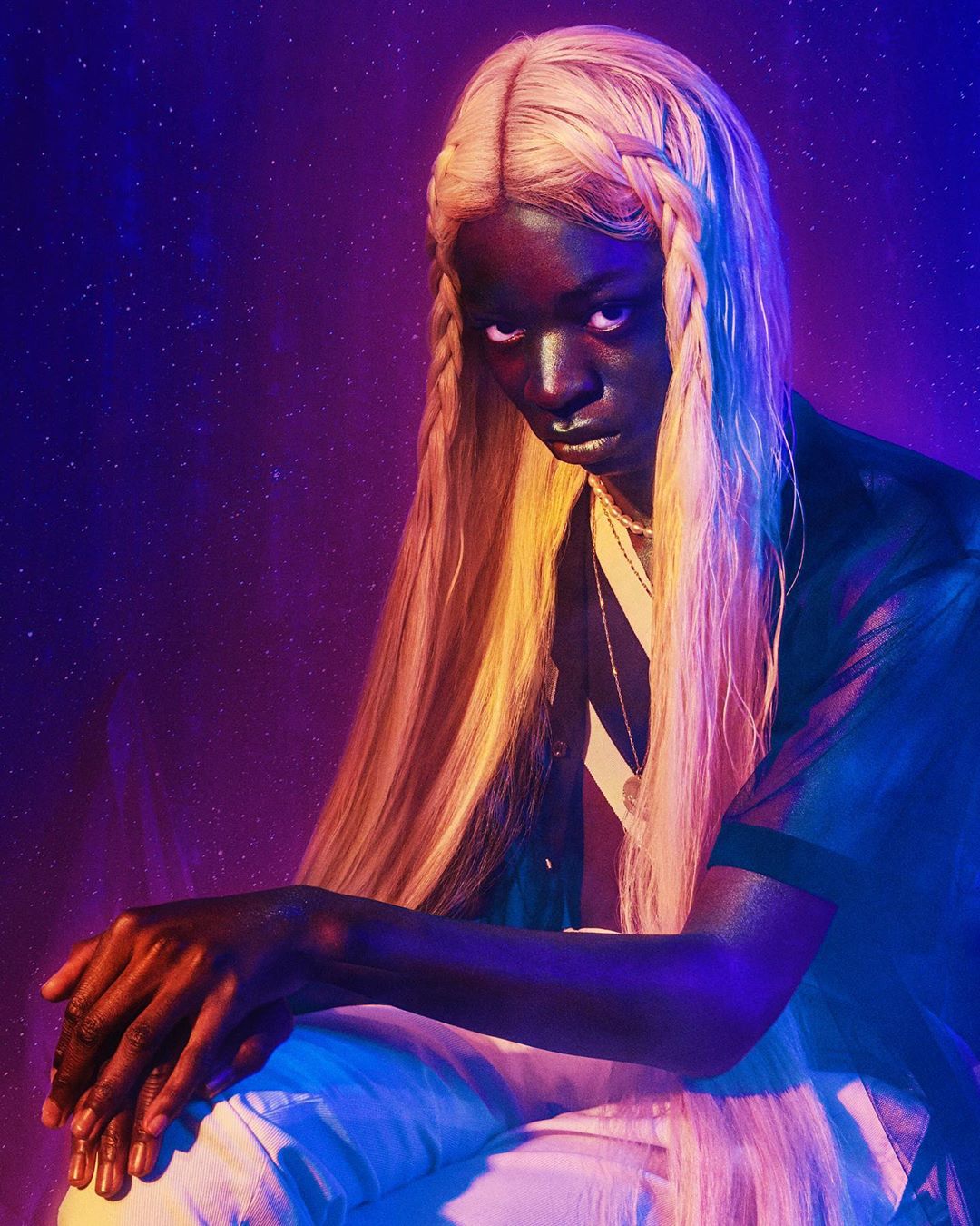 Portrait of a black adult female with braided blonde hair looking at the camera in a photo studio with purple and blue lighting.