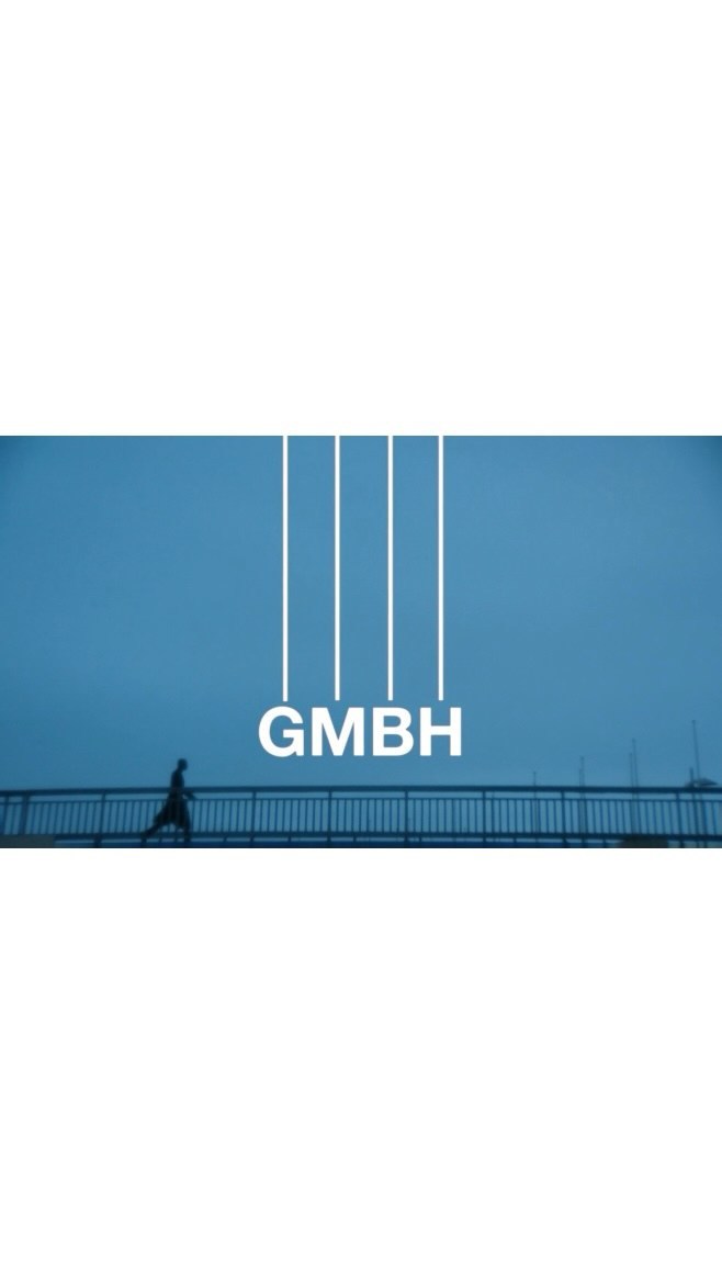Person walking on a bridge under a blue sky with 'GMBH' text. Minimalist style with a distant horizon, creating a sense of scale.