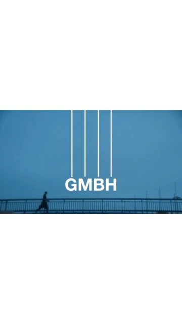 Person walking on a bridge under a blue sky with 'GMBH' text. Minimalist style with a distant horizon, creating a sense of scale.