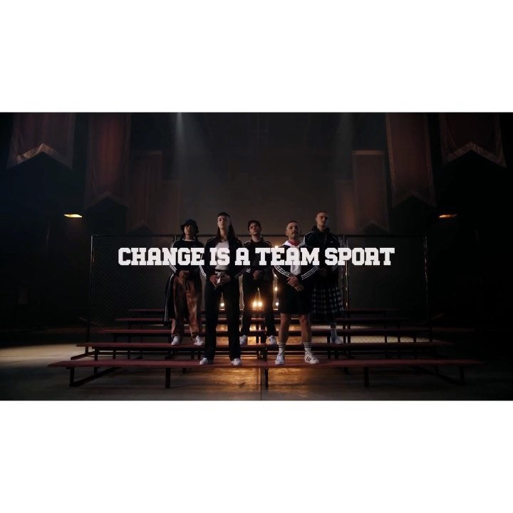 Group of five diverse adults standing on bleachers in a dimly lit indoor venue with the text: CHANGE IS A TEAM SPORT.
