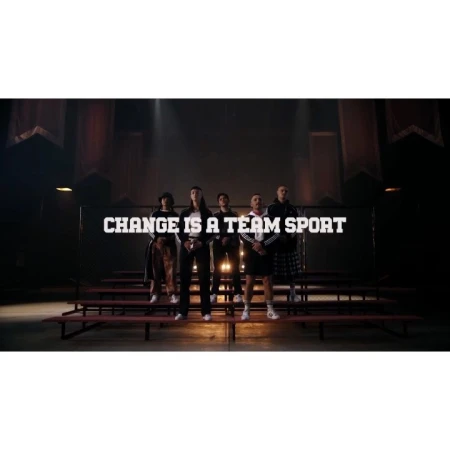 Group of five diverse adults standing on bleachers in a dimly lit indoor venue with the text: CHANGE IS A TEAM SPORT.