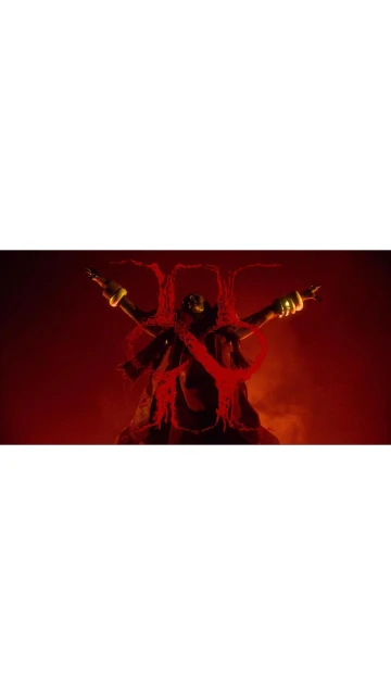 Figure in dark robe and gold accessories stands with arms outstretched against a deep red background, creating a dramatic visual.