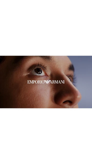 Macro shot of a person's face featuring their eyes looking upwards, with the Emporio Armani logo centrally placed on their skin.