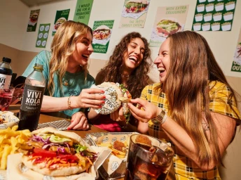 Three young women laughing together in a restaurant while sharing food and drinks, photographed by Matteo Rolfi.
