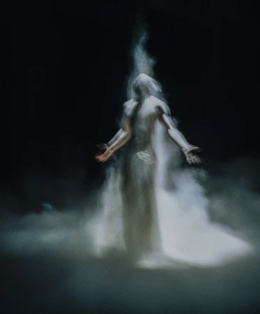Abstract ethereal figure in white smoke against a dark background, with arms outstretched in a gesture of reaching or offering.