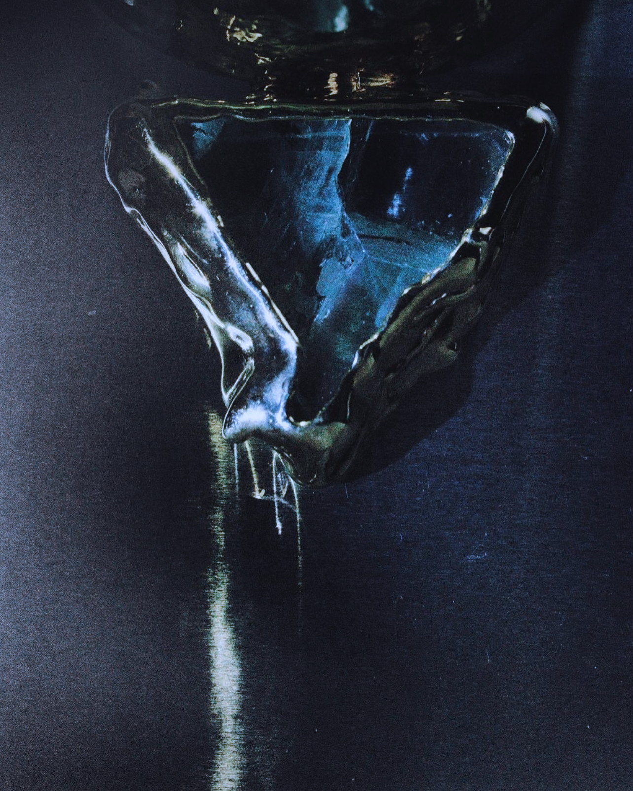 Abstract still life of a reflective, dark triangular object with liquid, creating depth and highlights in a dark blue and black color palette.