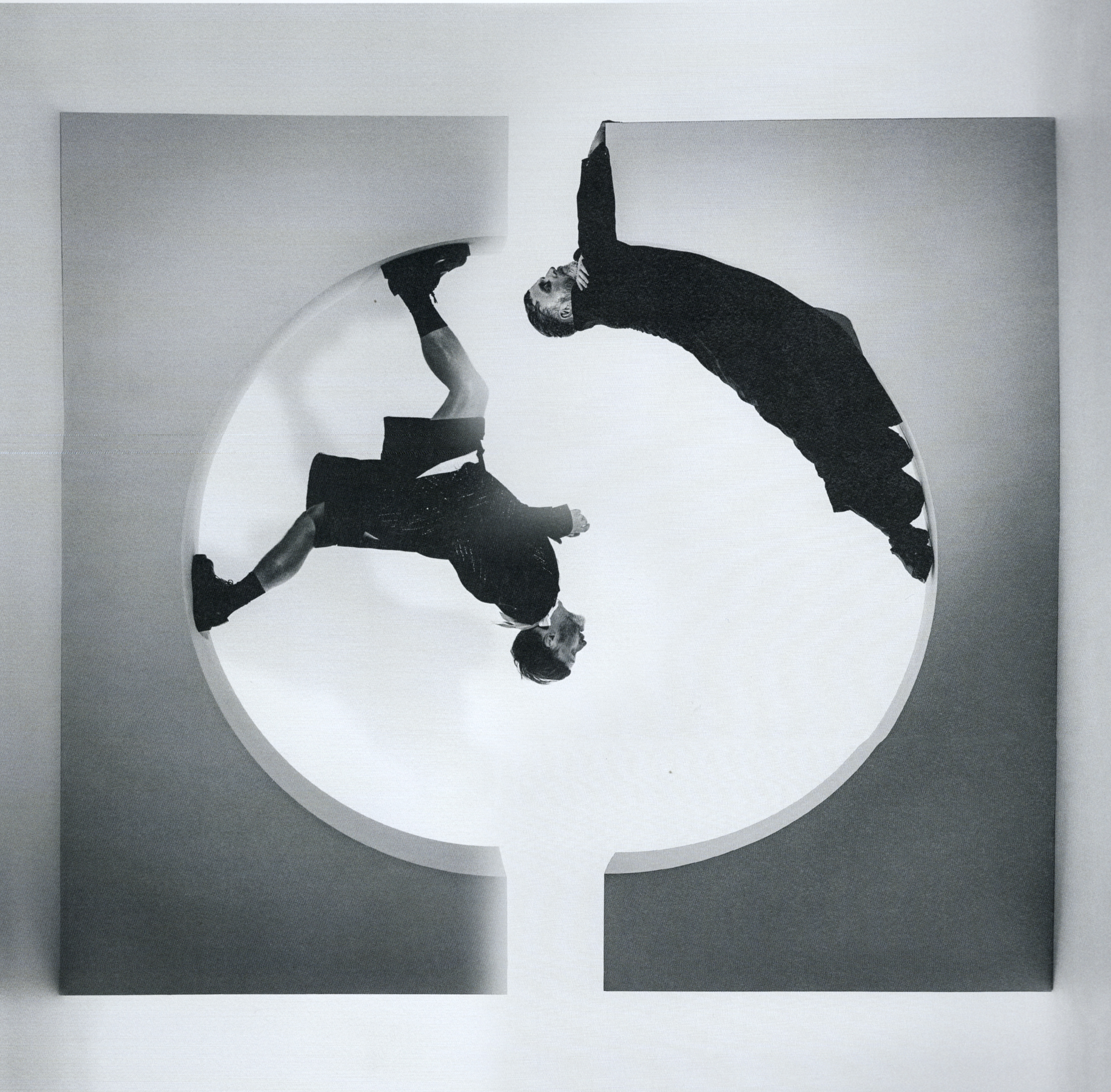 Monochrome image featuring two figures in dark suits dynamically posed against a geometric backdrop, creating an abstract visual composition.