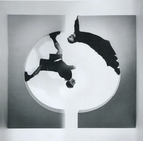 Monochrome image featuring two figures in dark suits dynamically posed against a geometric backdrop, creating an abstract visual composition.