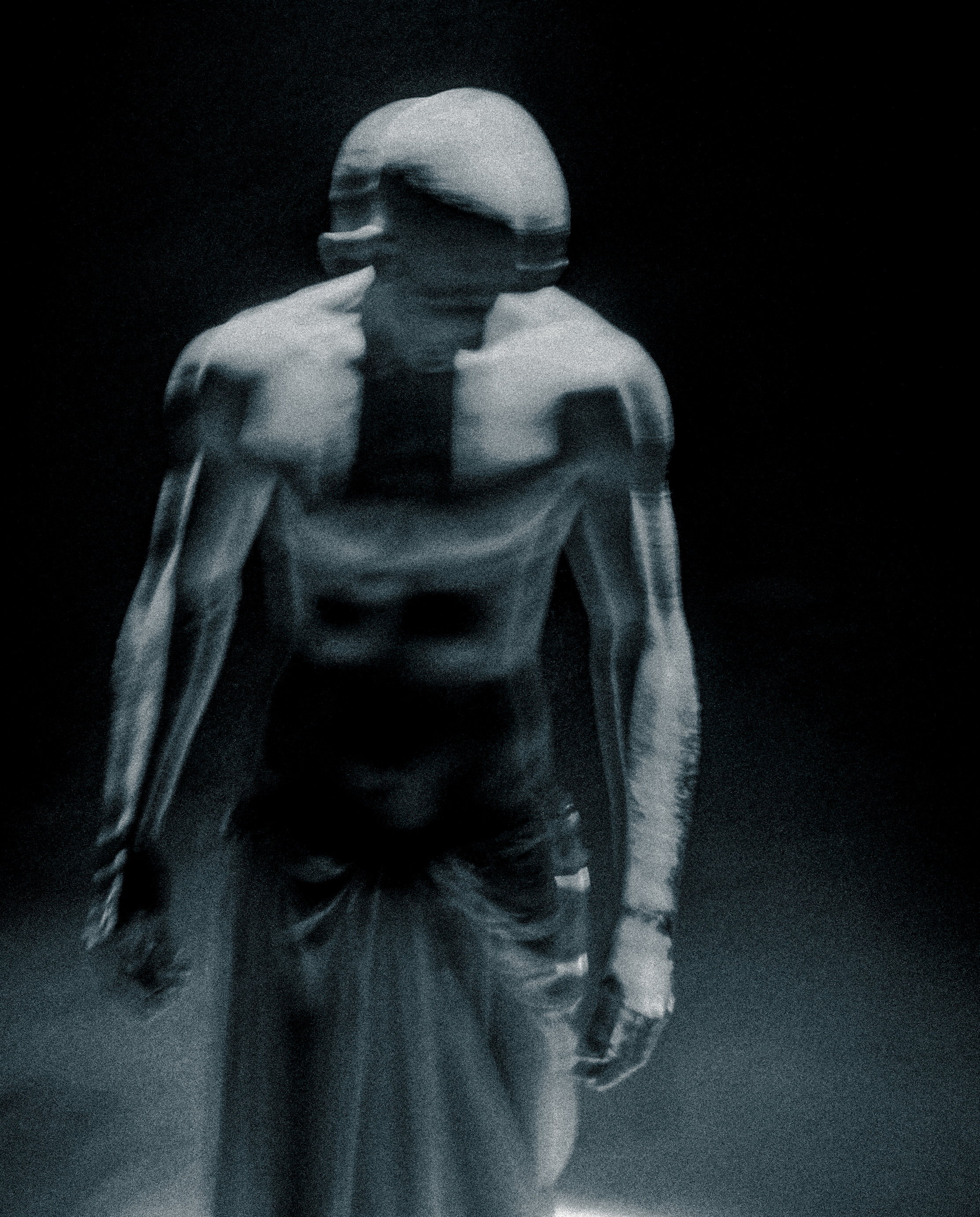 Surreal studio shot of an adult male figure in partial shadow with strong musculature, posing with an otherworldly or statue-like aesthetic.