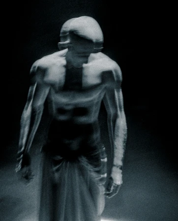 Surreal studio shot of an adult male figure in partial shadow with strong musculature, posing with an otherworldly or statue-like aesthetic.