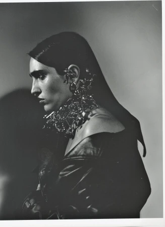 Monochrome portrait of a woman with dark hair, wearing an off-the-shoulder top and striking metal jewelry. Dramatic lighting.