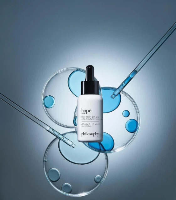 Beauty product shot of Philosophy Hope in a Jar serum bottle with dropper on petri dishes, set against a gradient blue background.