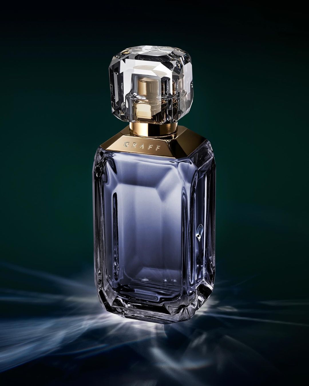 Close-up studio shot of a crystal perfume bottle with gold accents against a dark green background with refracted light patterns.